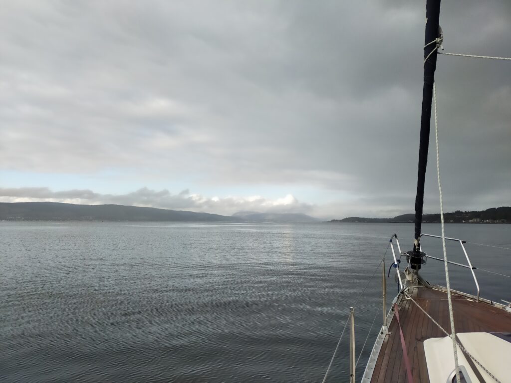 A view up the Firth of Clyde with the bow of the boat and cloud moving in. There are only the faintest ripples disturbing the water.